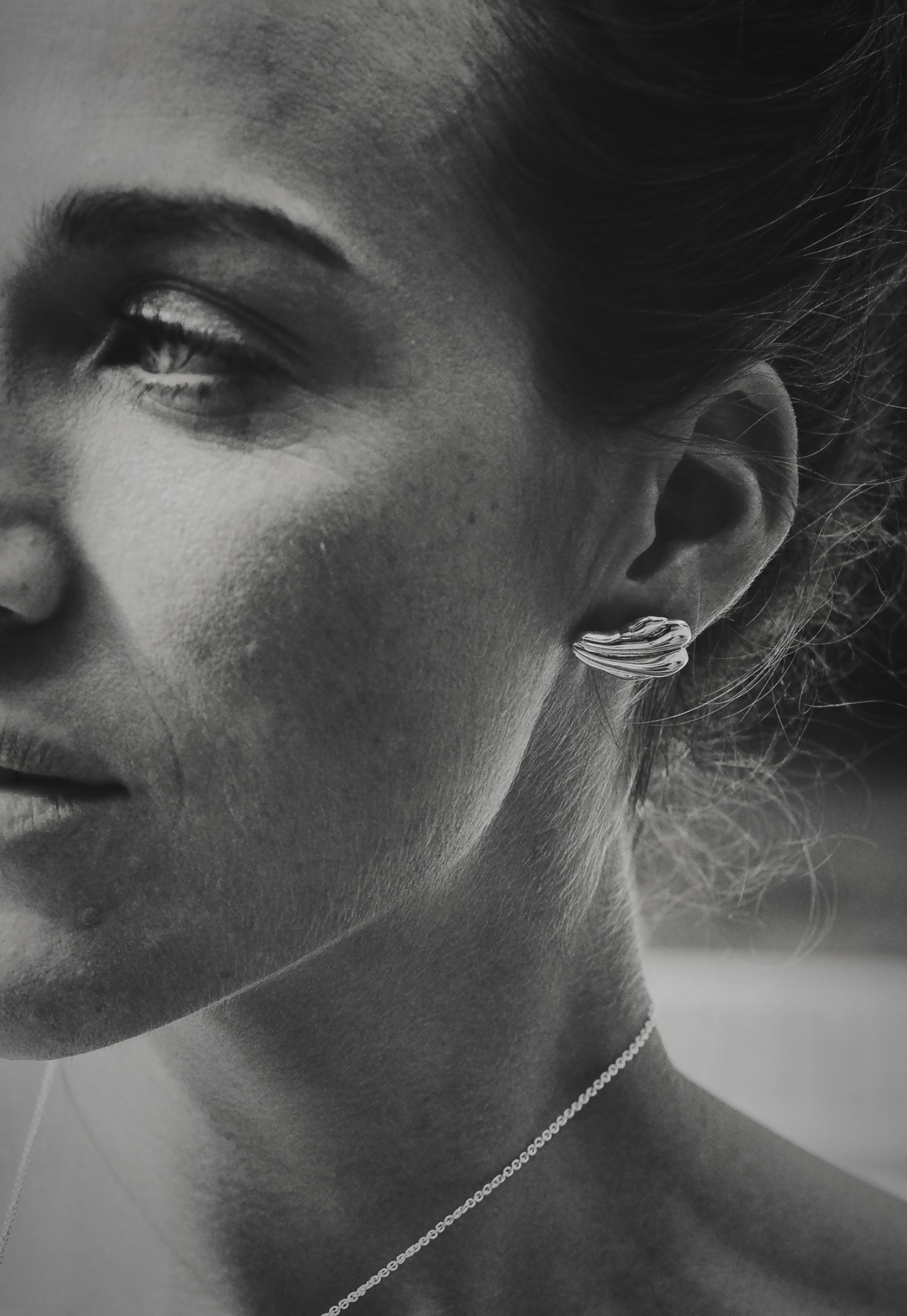 Black & white image of close up of shell fragment earrings in silver, on model, eye shown and edge of mouth.